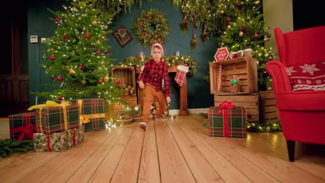 Junge-Mit-Weihnachtsmütze-Rutscht-Vor-Glück-Im-Weihnachtlich-Dekorierten-Wohnzimmer-Auf-Den-Boden