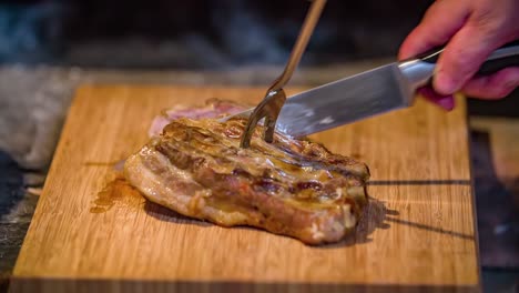 Close-up-of-a-person-slicing-a-juicy-piece-of-pork-meat-on-a-wood-board