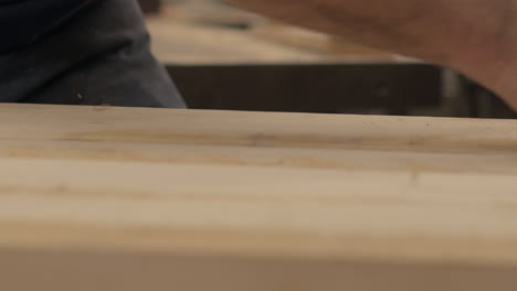 Craftsman-runs-a-planer-over-wood-boards,-side-view-in-slow-motion
