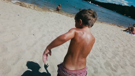 POV-as-camera-chases-little-boy-around-on-a-sandy-beach-on-summer-day