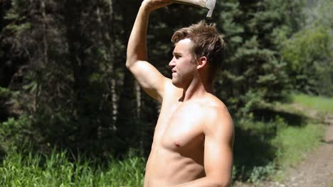 Slow-motion-shot-of-a-shirtless-man-practicing-his-axe-throwing-skill-by-trying-to-throw-his-hatchet-at-a-pine-tree