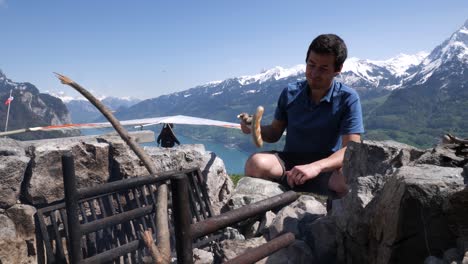 Slow-motion-shot-of-a-young-man-grilling-a-sausage-over-a-bonfire-while-a-delta-sailer-starts-in-the-background-over-a-beautiful-Swiss-lake-in-the-alps-of-Switzerland