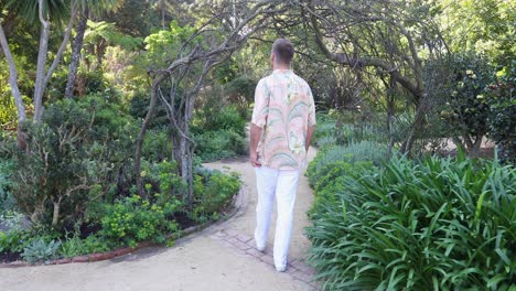 Young-male-in-hawain-shirt-walks-through-wooden-archway-in-garden_slow-motion