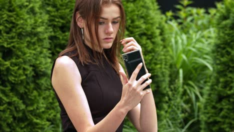 Girl-in-black-dress-fixing-her-hair-using-smartphone-as-a-mirror