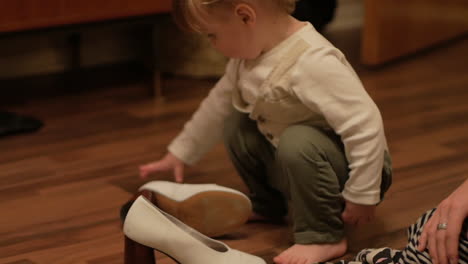 A-Cute-Chubby-Toddler-Fixing-A-White-Heeled-Shoes-On-The-Wooden-Floor---Close-Up-Shot