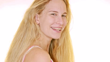 Against-a-white-backdrop,-a-young-blonde-woman-looks-over-her-shoulder-and-giggles