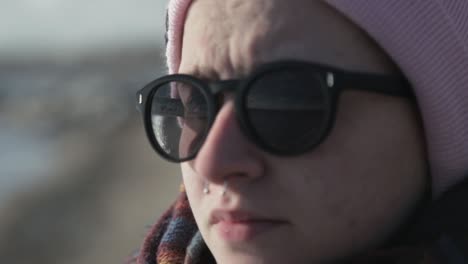 Gorgeous-Caucasian-Lady-Wearing-Sunglasses-And-With-A-Septum-Piercing-Staring-Somewhere-By-The-Lake-Shore-In-Canada-On-A-Sunny-Day---Closeup-Shot