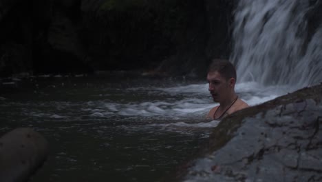 Ein-Junger-Mann,-Der-Auf-Dem-Kalten-Wasser-Schwimmt-Und-Sich-Entspannt,-Das-Von-Den-Wunderschönen-Wasserfällen-Fließt---Weitschuss