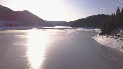 Sunlight-shines-and-reflects-on-frozen-mountain-lake-in-winter-with-snow-on-landscape