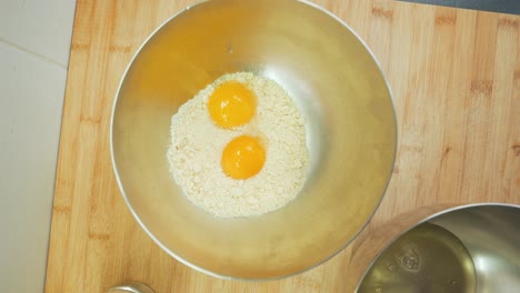 Cracking-two-eggs-into-flour-in-mixing-bowl,-making-and-baking-cake-mix-at-home