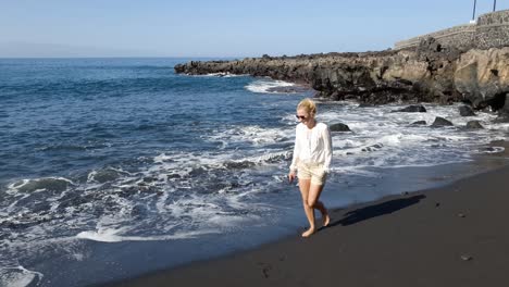 Mujer-Caucásica-Caminando-En-La-Playa-De-Arena-Negra-De-Tenerife,-Islas-Canarias,-España