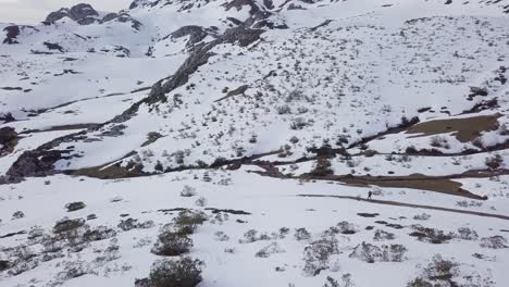 Aerial-view-over-snowy-mountains-and-hiker-walking-on-path-in-winter