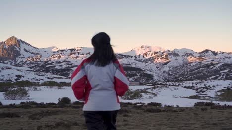 A-woman-walks-in-slow-motion-towards-a-range-of-snow-capped-mountains-in-the-winter-season