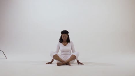 Black-woman-with-bowed-head-and-crossed-legs,-looks-forward-then-places-her-hands-on-her-knees-with-fingers-in-a-mudra-for-meditation