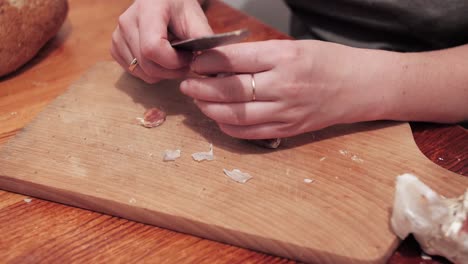 Woman's-hands-with-a-knife-crush-the-garlic-on-a-chopping-board,-then-peel-the-skin