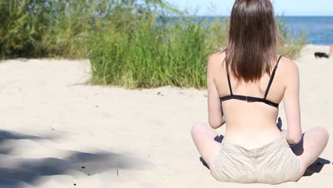 Rear-view-of-young-woman-sitting-on-sandy-beach-in-sunny-summer-day