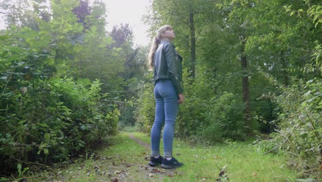 Girl-stands-on-nature-path-and-stares-up-in-wonder,-low-angle