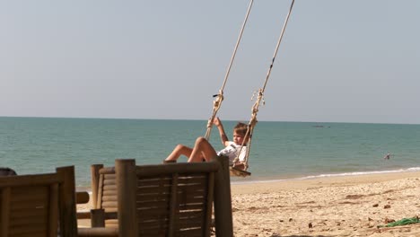Slow-motion-of-Child-on-tree-swing-on-tropical-beach,-ocean-horizon-in-background