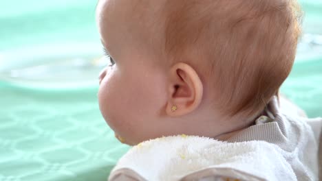 A-curious-baby-wearing-a-bib-stares-into-the-camera-and-then-turns-its-head,-slow-motion-shot