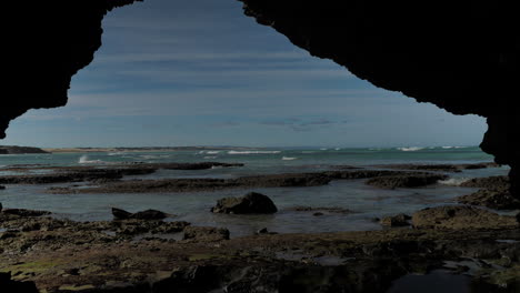 Tilt-up-shot-from-cave,-revealing-coastline-and-waves,-with-child-walking-across-frame
