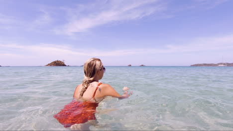 Young-Beautiful-Woman-sits-in-the-crystal-clear-oceans-of-Nacpan-Beach-in-El-Nido-Philippines-as-the-camera-pans-round,-perfect-holiday-and-dream-destination