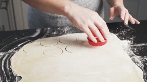 Lady-using-a-cookie-cutter-to-cut-shapes-of-dough-rolled-out-on-her-counter