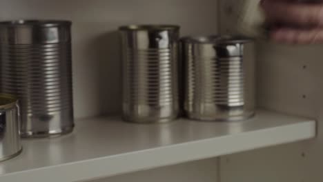 Stacking-aluminum-tin-cans-out-of-food-cupboard-shelf