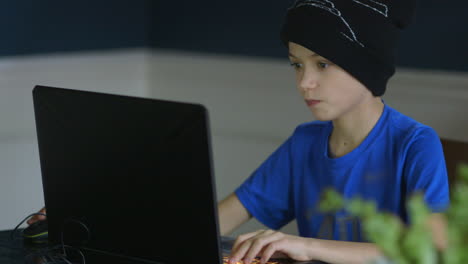 Young-boy-playing-games-on-a-laptop-computer-in-the-dining-room-medium-shot