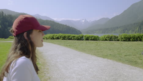 A-young-woman-wearing-a-baseball-cap-looks-toward-the-majestic-mountains-in-the-background,-then-turns-and-smiles-at-the-camera