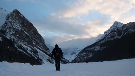 Hombre-Caminando-Sobre-Un-Lago-Congelado-Con-Montañas-De-Fondo