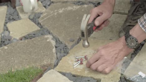 Workman-hands-hammering-nails-into-nail-hook-cable-clip-on-concrete-floor