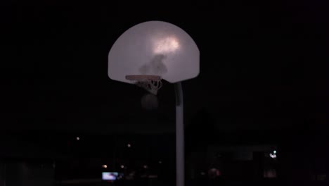Teenage-girl-runs-up-and-shoots-a-basket-at-an-outdoor-court-in-the-dark