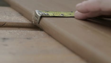 Workman-hand-using-metal-tape-measure-to-measure-piece-of-wood