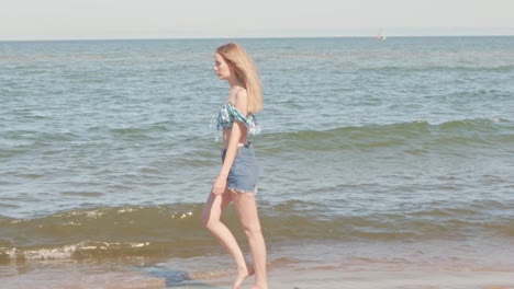 Young-blond-woman-walking-on-beach-on-shoreline