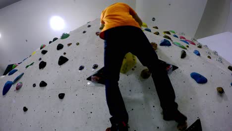 Boulder-gym-climbing-wall-seen-right-from-below-as-a-climber-approaches-and-climbs-up-and-then-down-with-no-rope