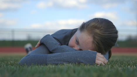A-girl-athlete-lays-down-in-the-grass-of-a-high-school-football-field