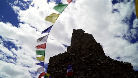 Banderas-De-Oración-Tibetanas-En-El-Viento-En-Las-Ruinas-Del-Monasterio-Budista-En-El-Himalaya,-Cámara-Apuntando-Hacia-Arriba