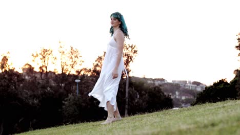 Flowing-blue-hair-and-white-dress,-barefoot-Gen-Z-woman-spinning-on-grass-at-twilight---SLOMO