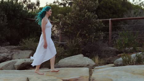 Tranquility---woman-in-white-dress-and-blue-hair-walks-barefoot-on-rocks-in-twilight,-SLOMO