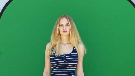 Static-medium-shot-of-a-blonde-lady-model-posing-in-front-of-a-chroma-key-with-a-blank-facial-expression