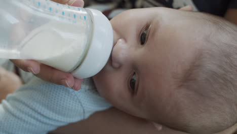 Nahaufnahme-Eines-Babyboy-Säuglings,-Der-Seine-Mahlzeit-Aus-Der-Flasche-Mit-Babynahrung-Aus-Mutterhänden-Hat