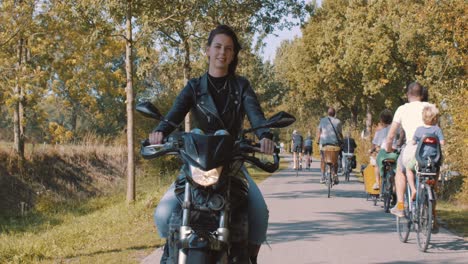 Frau,-Die-Im-Herbst-In-Der-Natur-Motorrad-Fährt-Und-Lederjacke-Trägt,-Die-Auf-Der-Straße-Vorbeifahrende-Radfahrer-Fährt