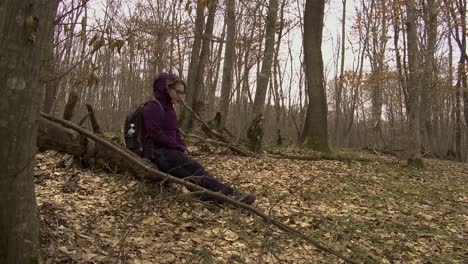 Low-angle-side-view-of-woman-in-forest-sitting-on-a-fallen-tree-to-rest