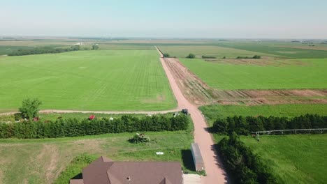 Aerial-drone-view-following-a-gravel-road-out-of-a-farm-yard-along-a-soybean-field