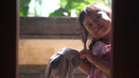 Sweet-little-Indonesian-girl-smiles-through-a-window-as-she's-cleaning