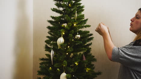 Mujer-Joven-Colgando-Adornos-Decorativos-De-Vidrio-En-Un-árbol-De-Navidad-Artificial