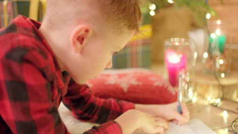 Young-boy-is-laying-on-the-floor,-writing-his-wish-list-for-Christmas