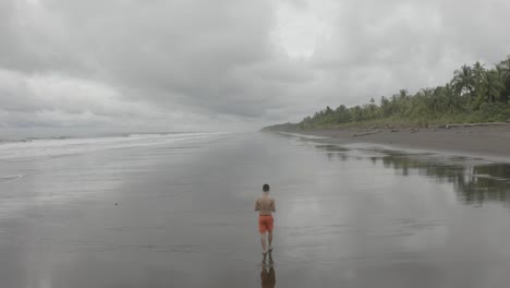 Aerial-flying-over-a-young-guy-walking-at-an-empty-Beach-in-Colombia