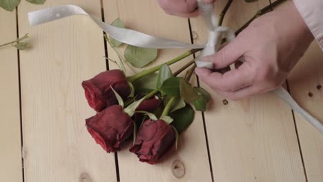 Hands-tying-ribbon-bow-round-bouquet-of-red-roses
