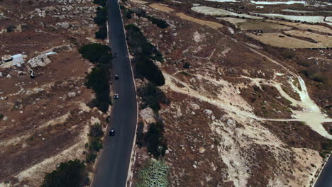 Aerial-Following-Group-Quad-Biking-Down-Road-In-Rugged-Landscape-Gozo,-Malta